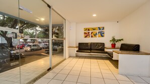 A reception area with a glass door, a sofa, a small table, and a potted plant. - Piratas da Praia Fit Hostel (Recife)