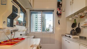 A compact kitchen with a window, a microwave, a stove, and a small countertop. - Piratas da Praia Fit Hostel (Recife)