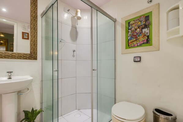 A bathroom with a glass-enclosed shower, a white sink, a toilet, and a framed artwork on the wall.