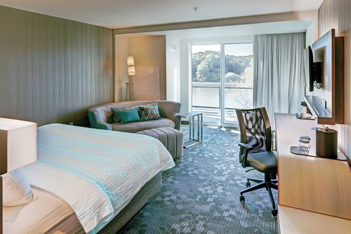Une chambre d’hôtel équipée d’un lit, d’un bureau, d’une chaise, d’une télévision et d’une grande fenêtre donnant sur l’extérieur.