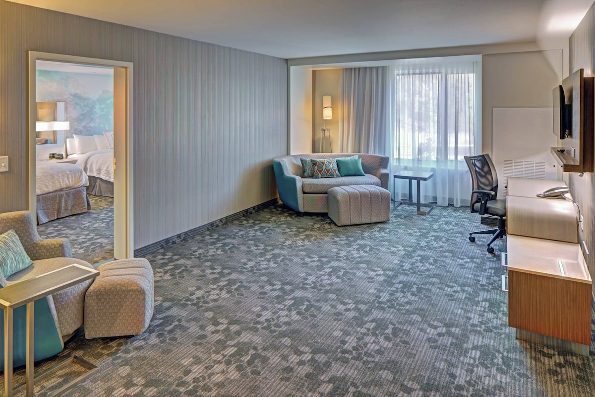 Une chambre d’hôtel équipée d’un canapé, d’un fauteuil, d’un pouf, d’un bureau et d’une télévision.