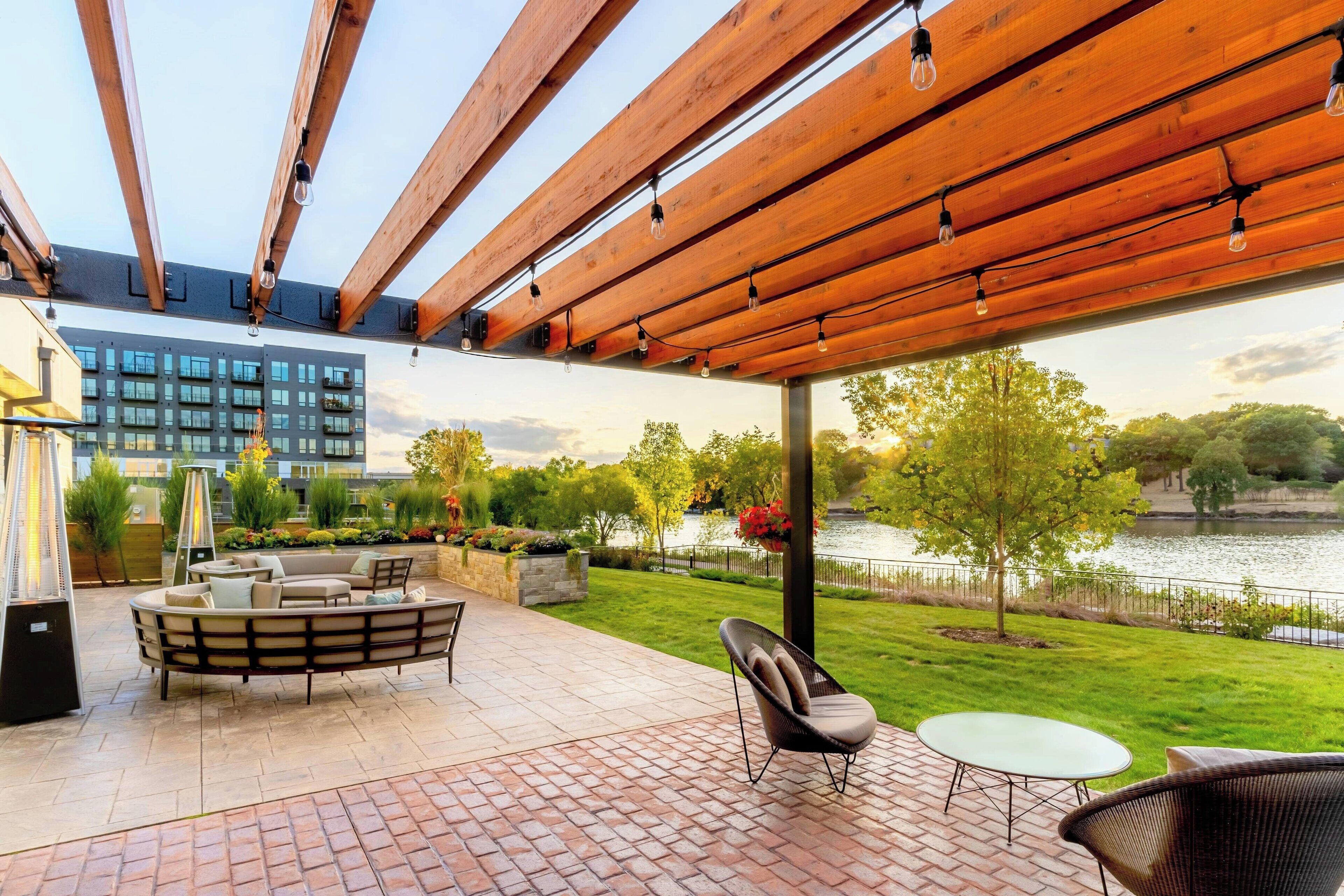 A covered patio with a brick floor, wooden ceiling beams, and outdoor furniture including a sofa and chairs.