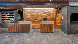 A reception area with wooden reception desks, a wall-mounted TV, and a snack vending machine. - Courtyard by Marriott Appleton Riverfront (Appleton)