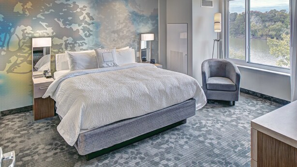 A modern hotel room with a large bed, a chair, a desk, and a view of the outdoors. - Courtyard by Marriott Appleton Riverfront (Appleton)