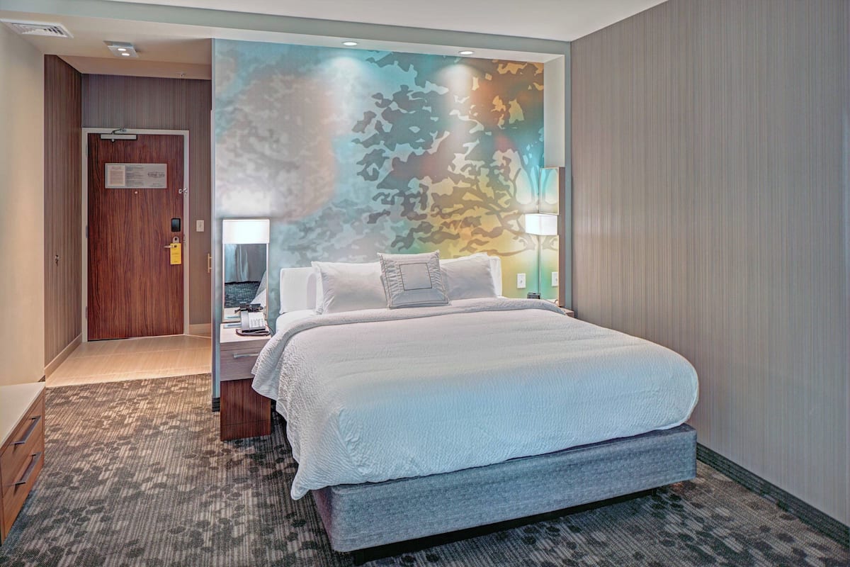 Une chambre d’hôtel avec un grand lit, une table de chevet, une lampe et un mur orné d’un motif de camouflage.