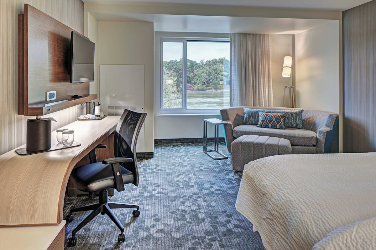 Une chambre d’hôtel équipée d’un bureau, d’un lit, d’un canapé et offrant une vue sur une étendue d’eau.