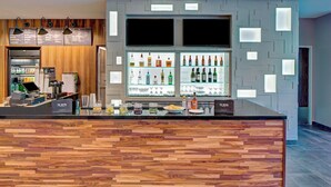 A modern bar area with a wooden counter, shelves of bottles, and a menu board. - Courtyard by Marriott Appleton Riverfront (Appleton)