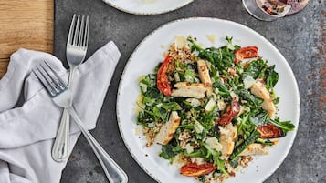 A plate of food with greens, tomatoes, and cheese on a table with a fork and napkin.