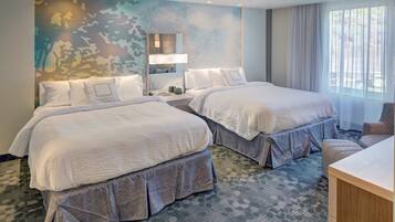 A hotel room with two beds, a large window with curtains, a wall mural, and a desk.