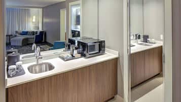 Un baño de hotel moderno con un lavamanos, un espejo y un microondas en la encimera.