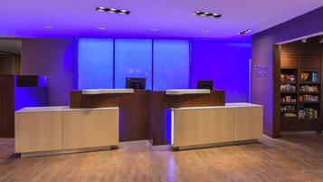 Un área de recepción con diseño moderno, que incluye un mostrador de recepción, una pantalla digital y un ambiente bien iluminado con iluminación ambiental azul.