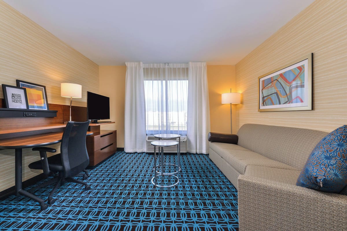 A hotel room with a desk, chair, sofa, and a patterned carpet.