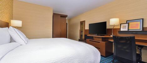 A hotel room with a large bed, a desk with a computer, a TV, and a chair.