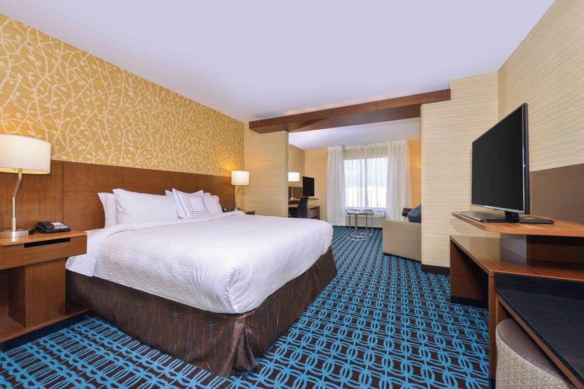 A hotel room with a large bed, a desk, a television, and a bathroom visible through an open door.