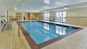 Una piscina interior con agua cristalina, paredes y suelo de azulejos. Hay sillones de descanso y una mesa con sillas alrededor de la piscina.
