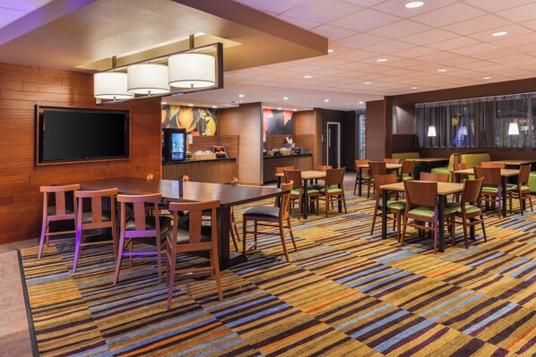 Un hall de hotel con una televisión grande, una recepción, varias zonas de estar y una alfombra estampada.