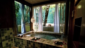 Une salle de bain avec une baignoire, une fenêtre avec des rideaux et un luminaire suspendu.