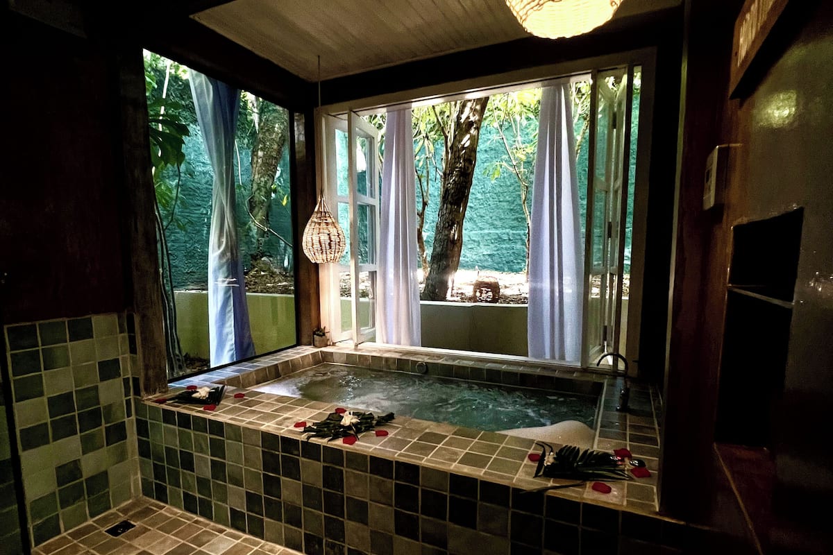 Une salle de bain avec une baignoire, une fenêtre avec des rideaux et un luminaire suspendu.