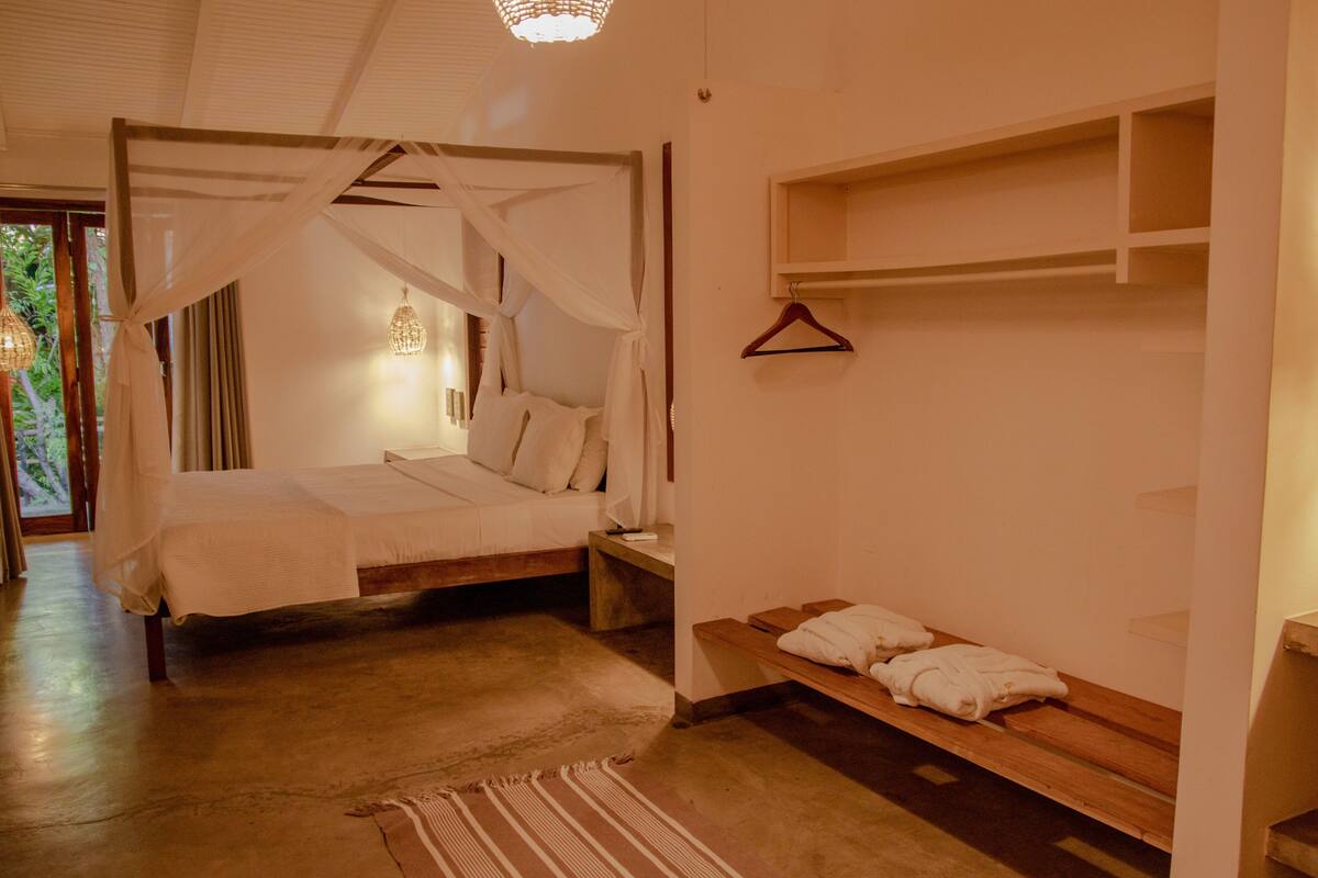 Une chambre à coucher avec un lit à baldaquin, un banc en bois avec des serviettes et un luminaire suspendu.