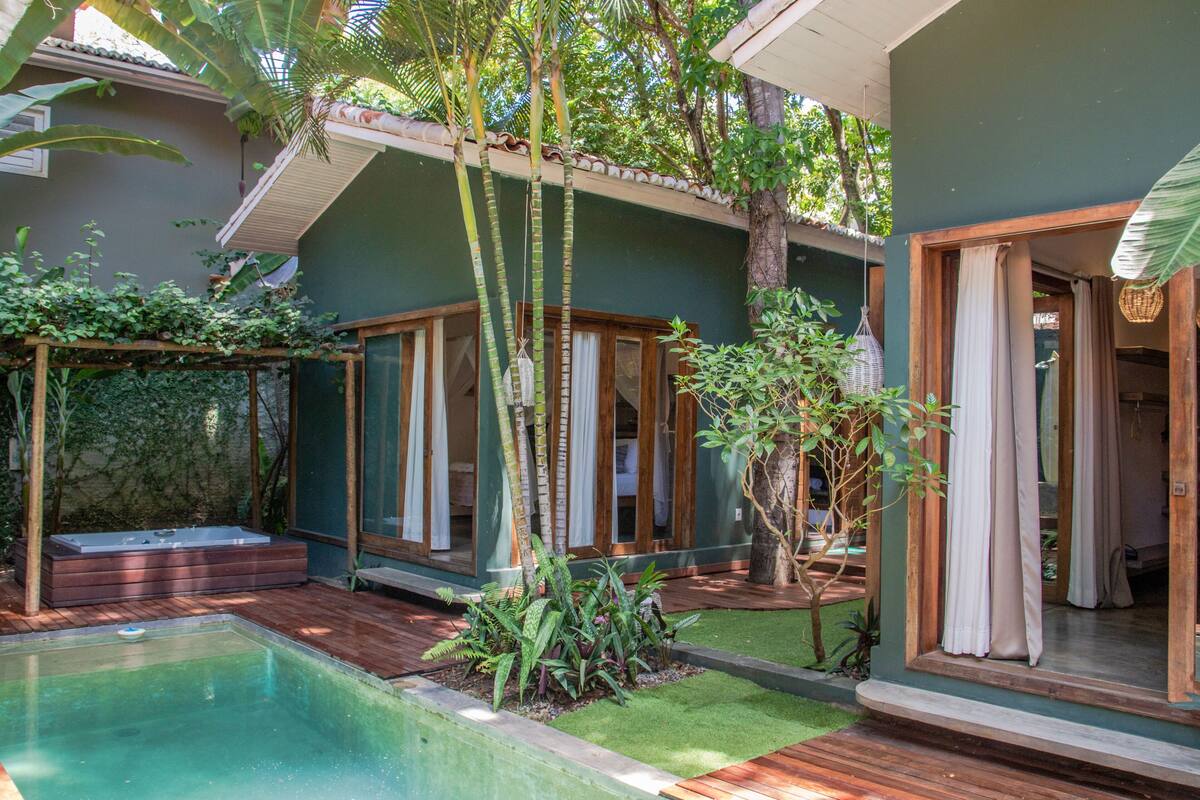 Un espace bien-être comprenant un jacuzzi, une terrasse en bois et une végétation luxuriante.