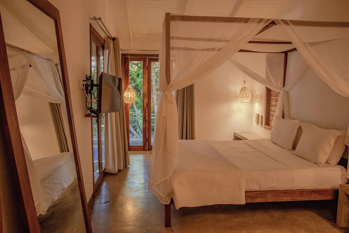 A bedroom with a canopy bed, a television mounted on the wall, and a view of the outdoors through a glass door.