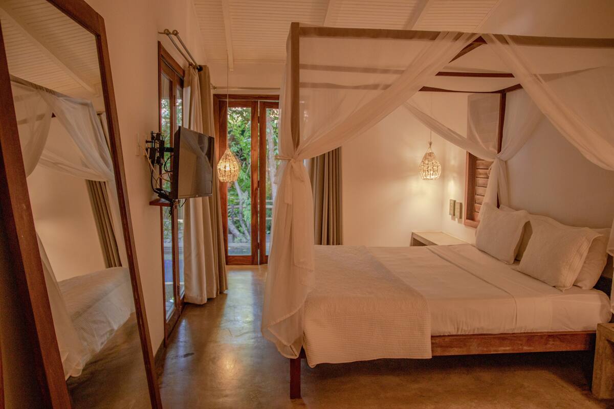 Une chambre à coucher avec un lit à baldaquin, un téléviseur fixé au mur et une vue sur l’extérieur grâce à une porte vitrée.