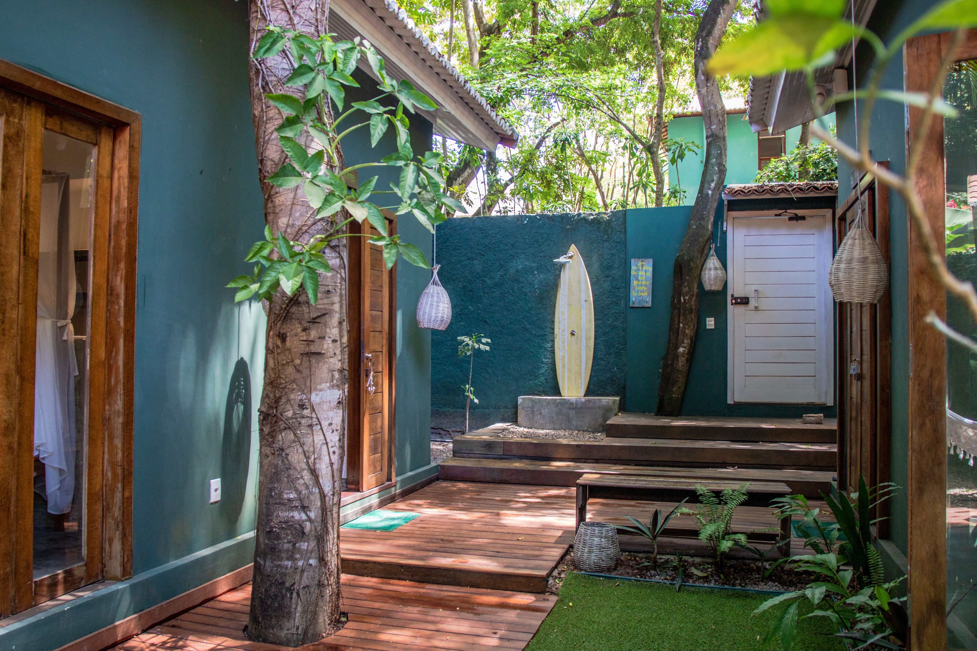 Una terraza de madera con un pequeño jardín, una puerta blanca y una decoración con una tabla de surf.