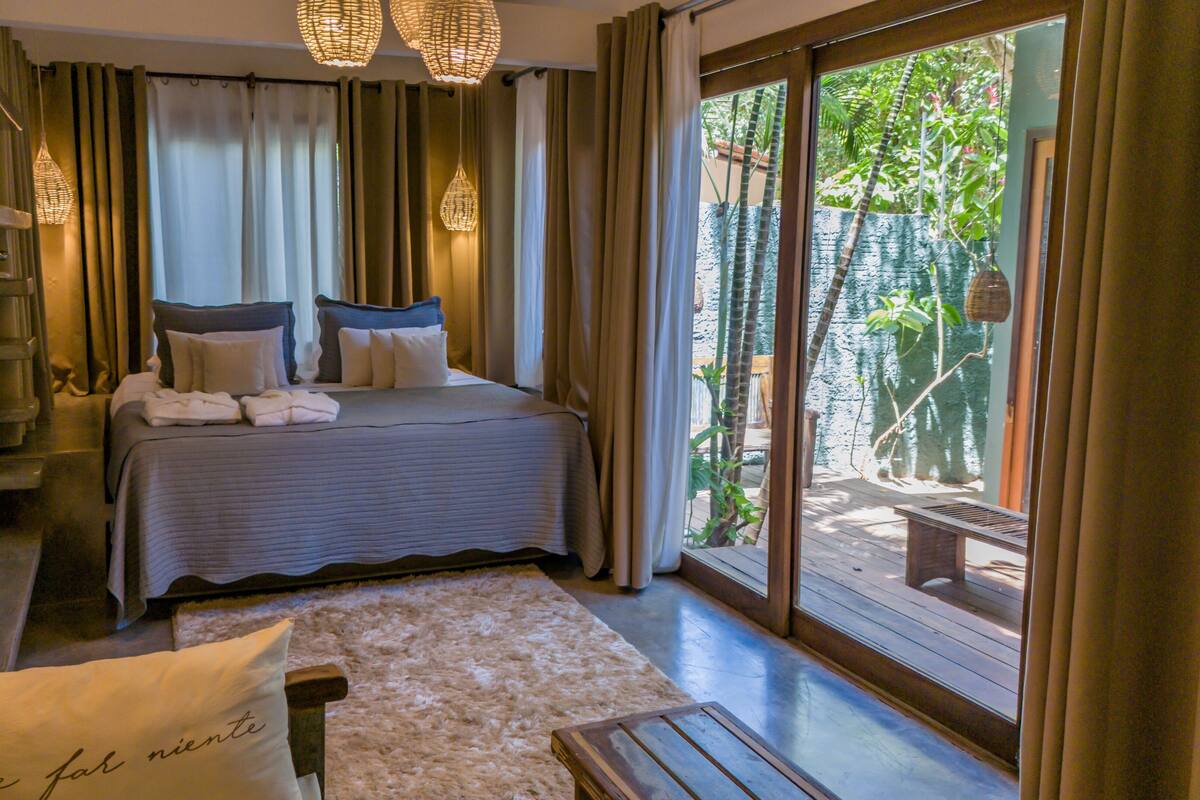 Une chambre d’hôtel avec un lit, un canapé, une fenêtre avec des rideaux et une vue sur la verdure.