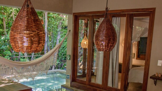 Un espace repas avec une table en bois dressée pour le repas, un jacuzzi et un hamac.