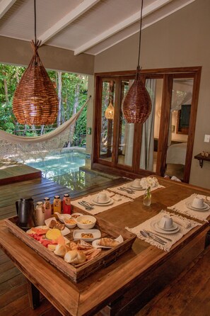 Un espace repas avec une table en bois dressée pour le repas, un jacuzzi et un hamac.