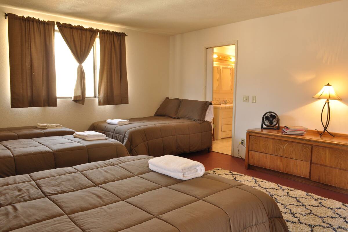 A hotel room with two beds, a wooden dresser, a lamp, and a view of the bathroom.