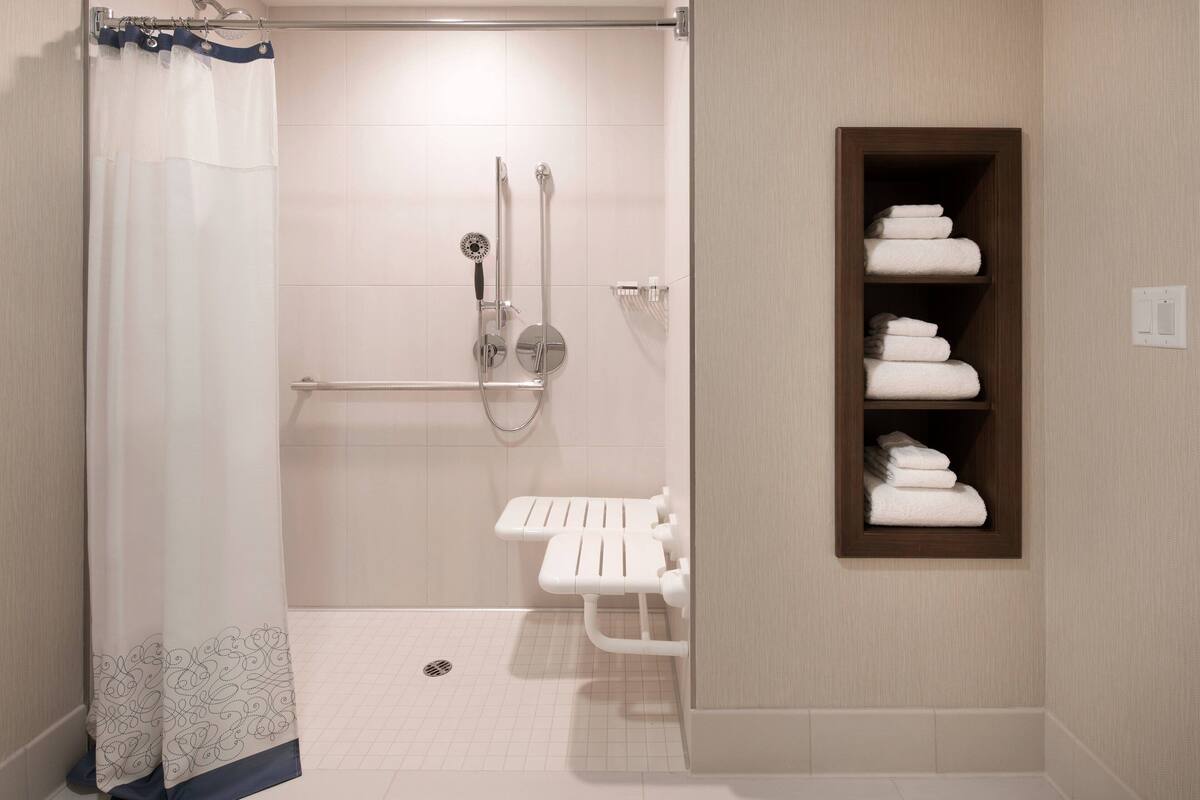 A bathroom with a shower, grab bar, and a shelf with towels.