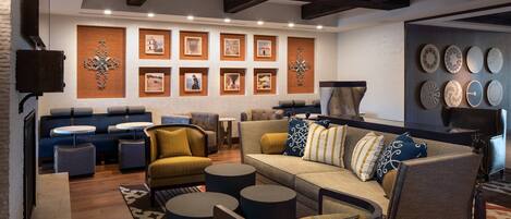 A modern living room with a sofa, armchairs, and round tables. There are framed pictures on the wall and a fireplace.