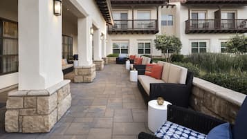 A covered outdoor patio with stone columns, wicker furniture, and a view of the building's exterior.