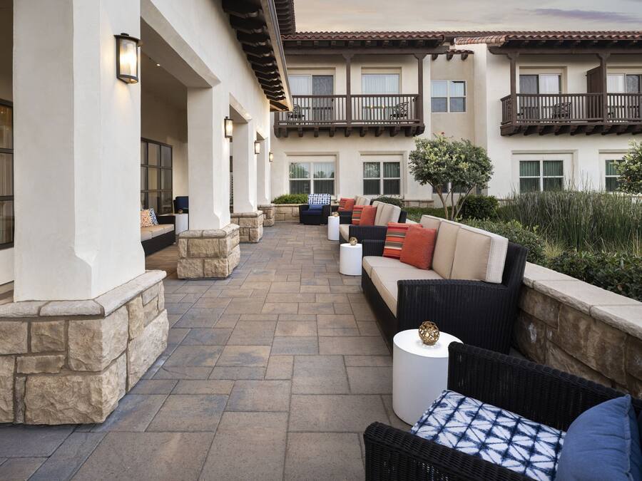 A covered outdoor patio with stone columns, wicker furniture, and a view of the building's exterior.