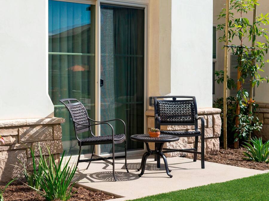 An outdoor patio with two metal chairs and a small table, surrounded by a stone wall and greenery.