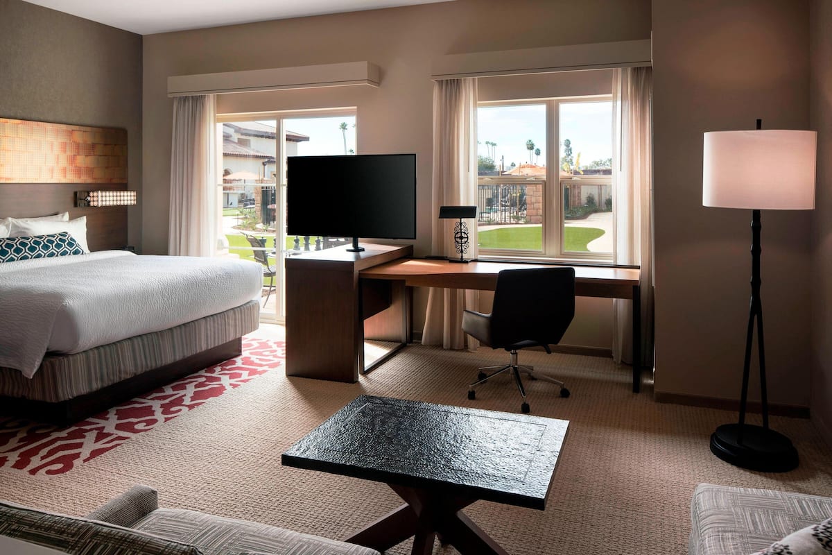 A hotel room with a bed, desk, chair, and a view of the outdoors.
