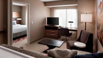 A hotel room with a bed, a desk with a TV, a chair, a sofa, and a lamp.