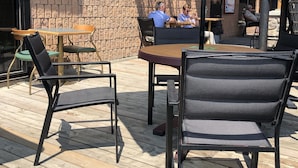 An outdoor seating area with tables and chairs, a brick wall, and a covered umbrella. - Companion Hotel Motel (Hearst)