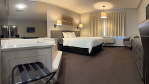 A hotel room with a large bed, a separate bathroom with a bathtub, a desk, and a chair. - Companion Hotel Motel (Hearst)