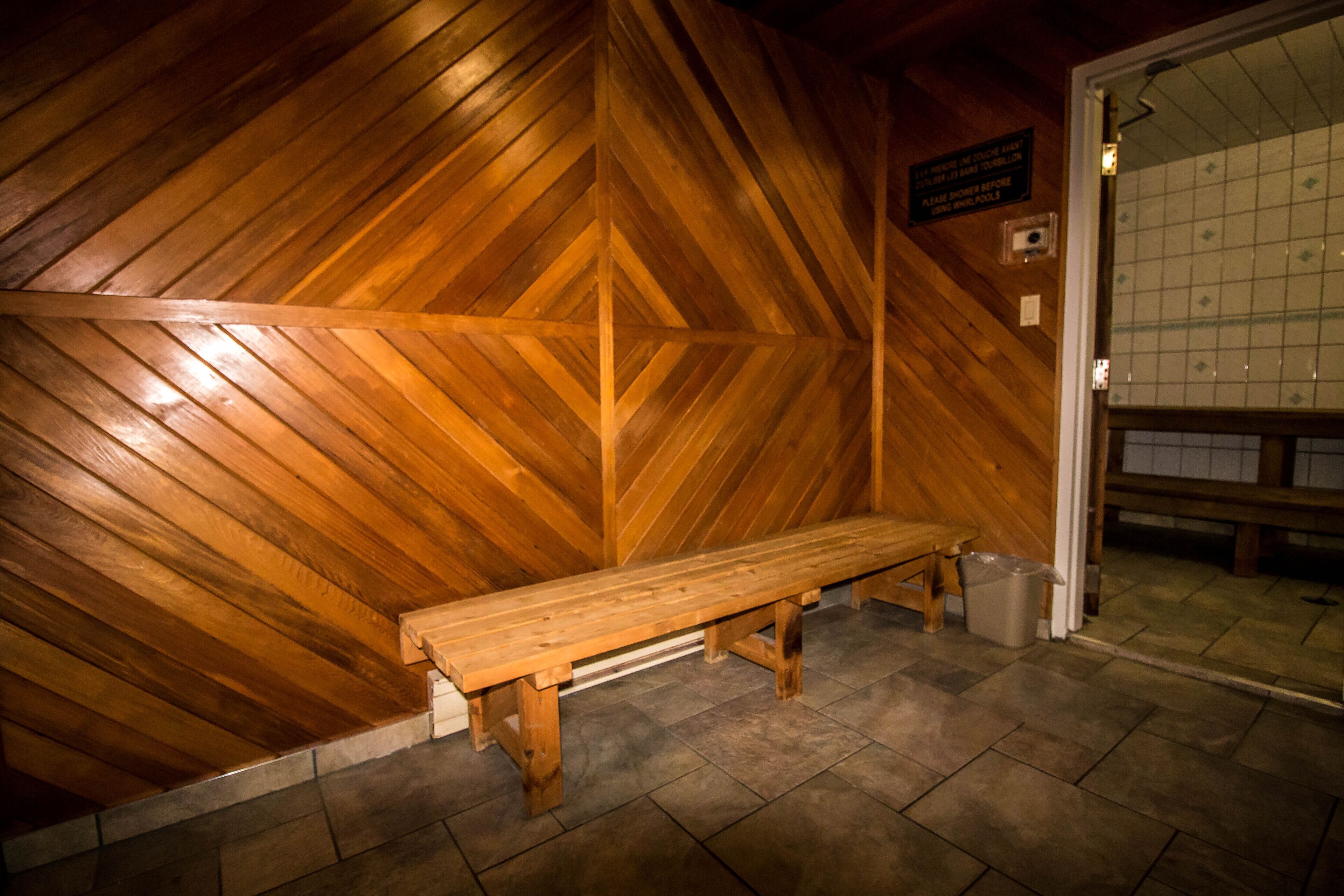 Un banc en bois dans une pièce dont le mur est décoré d’un motif en chevrons et dont le sol est carrelé.