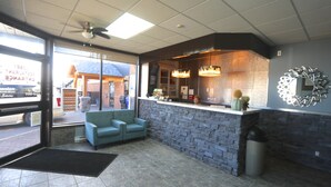 A reception area with a stone counter, a ceiling fan, and a large window. - Companion Hotel Motel (Hearst)