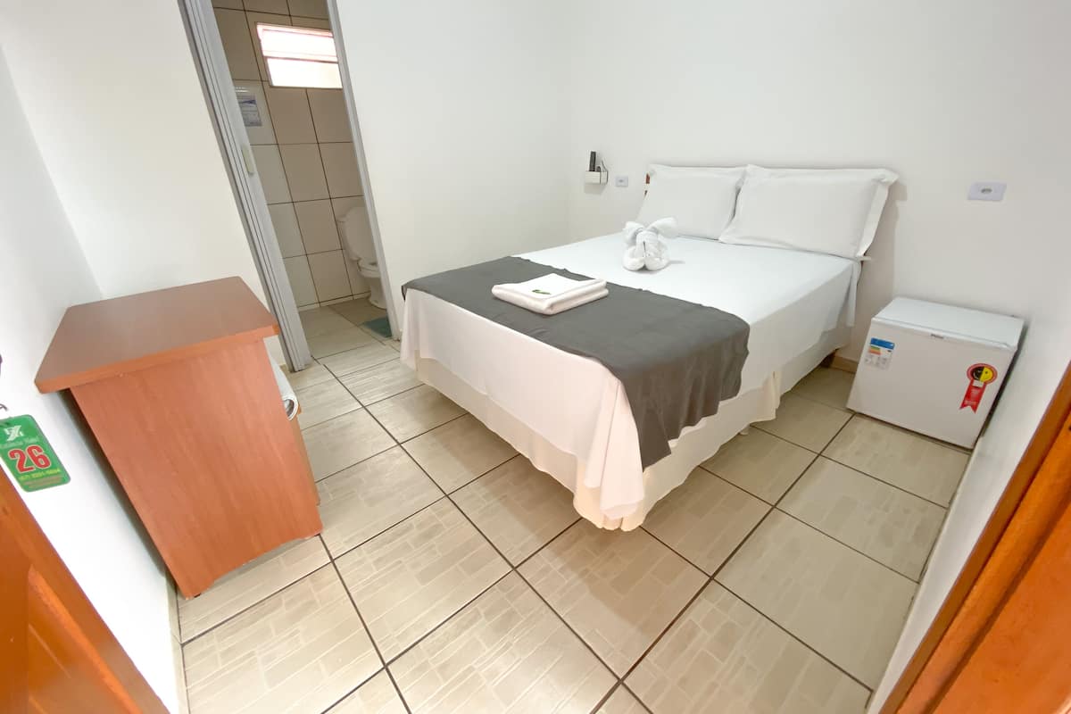 Una habitación de hotel con cama, un escritorio pequeño, un refrigerador y una puerta que da a un baño.