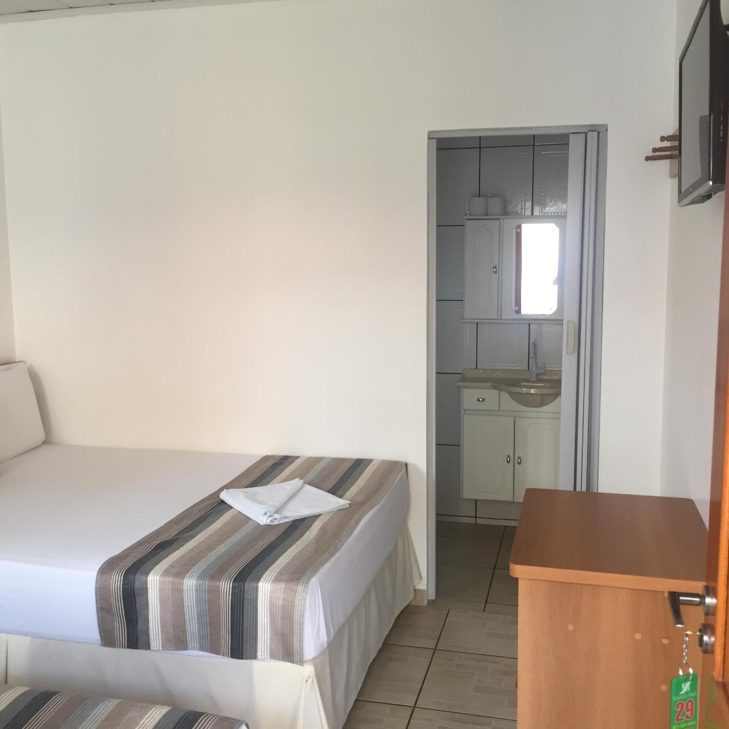 A bedroom with a bed, a bedside table, and a small kitchenette area with a sink and cabinets.