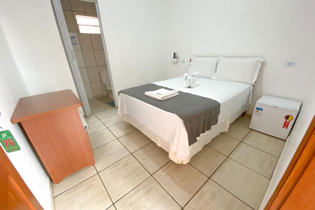 Una habitación de hotel con cama, un escritorio pequeño, un refrigerador y un baño visible a través de una puerta abierta.