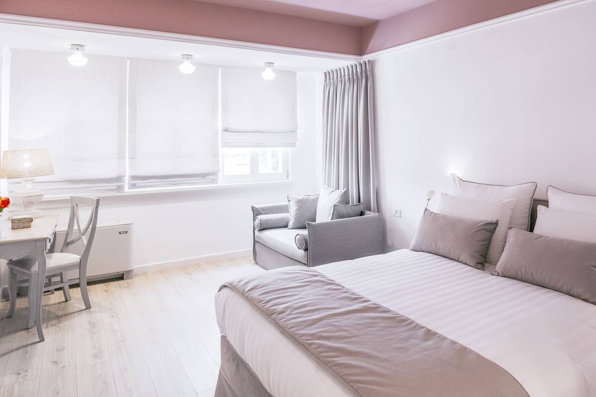 Una habitación de hotel moderna con una cama grande, un escritorio con lámpara y un ventanal con cortinas.