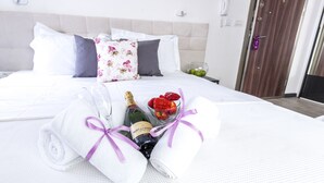 A neatly made bed with white linens and a bouquet of flowers and champagne. - Astera Apart Hotel (Skopje)