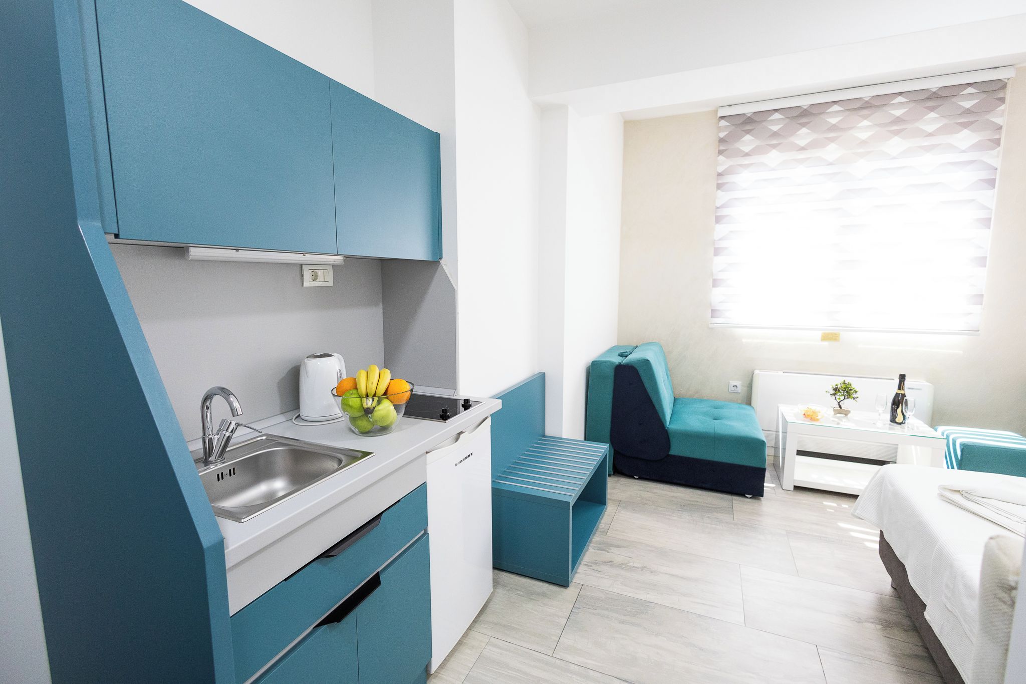 A compact kitchenette with a sink, a fruit bowl, and a small dining area with a bench and a table.