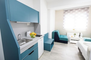 Una kitchenette compacta con un lavamanos, un frutero y una pequeña zona de comedor con un banco y una mesa.