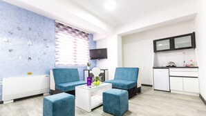 A modern living room with blue armchairs, a white coffee table, and a kitchen area with a refrigerator and microwave. - Astera Apart Hotel (Skopje)